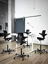 Der Sattelstuhl HAG Capisco Modell 8106 in Aktion an einem hohen Arbeitstisch.